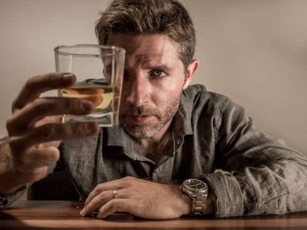alcoholic depressed and wasted addict man sitting in front of whiskey glass trying holding on drinking in dramatic expression suffering alcoholism and alcohol addiction isolated on grey background